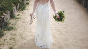 Mariée avec chaussures à la main marchant sur le sable