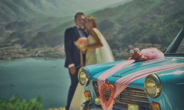 mariés posant pour une photo près d'une voiture bleue décorée avec rubans roses