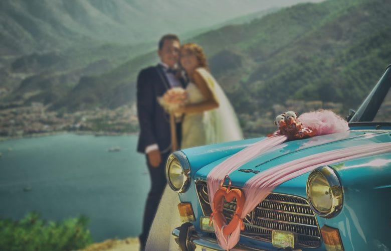 mariés posant pour une photo près d'une voiture bleue décorée avec rubans roses